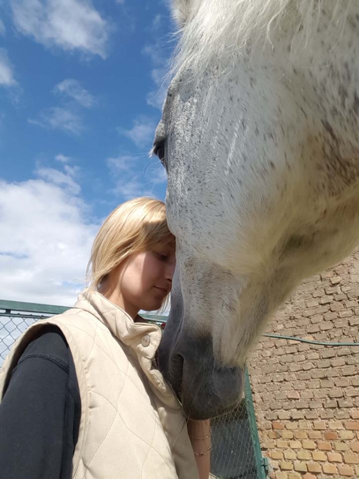 Myriam Blanc, front contre le chanfrein d'un cheval gris, les yeux fermés